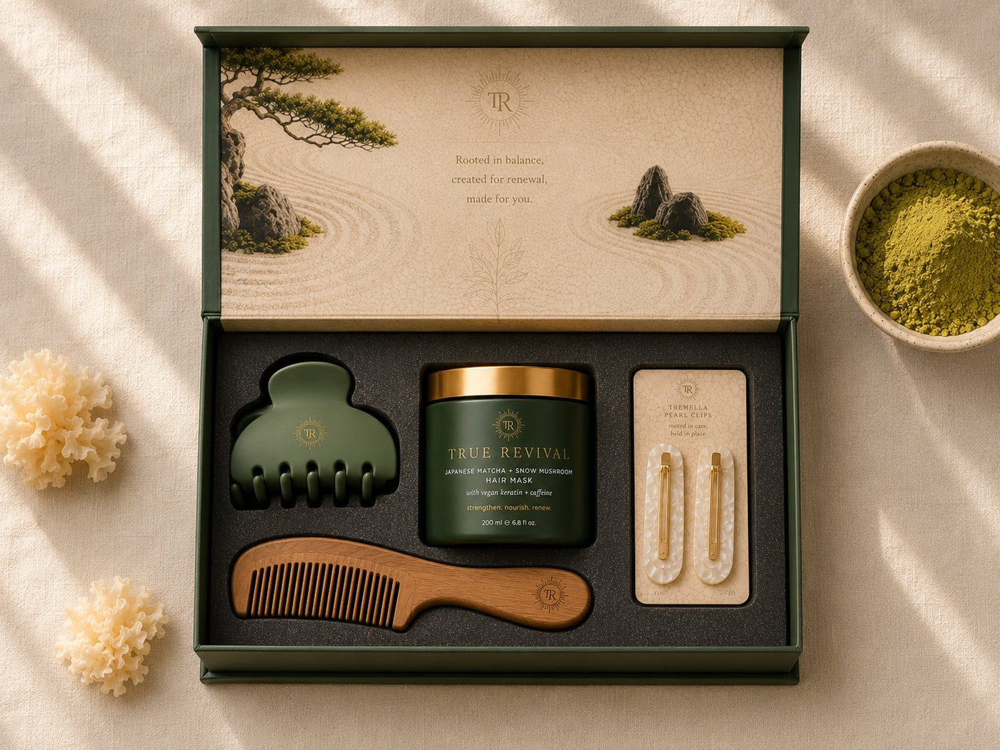 The open True Revival welcome kit: the hair mask jar, a sage claw clip, a wooden comb, and Tremella pearl clips set in the foam insert, beside matcha powder and snow mushroom